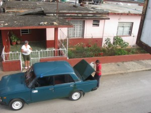 El chofer baja la mercancía y Manuela espera en la puerta.